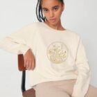 Sweat femme en coton biologique, col bateau. Couleur naturel du coton avec un dessin de fleurs sur le devant sérigraphié en doré.