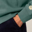 Sweat femme en coton biologique de couleur vert jade avec un dessin représentant les cinq éléments dans le dos de sérigraphie beige avec Logo de la marque sur la manche.